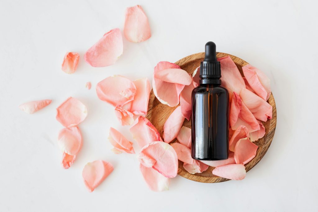 Beautiful essential oil bottle with rose petals arranged on wooden surface