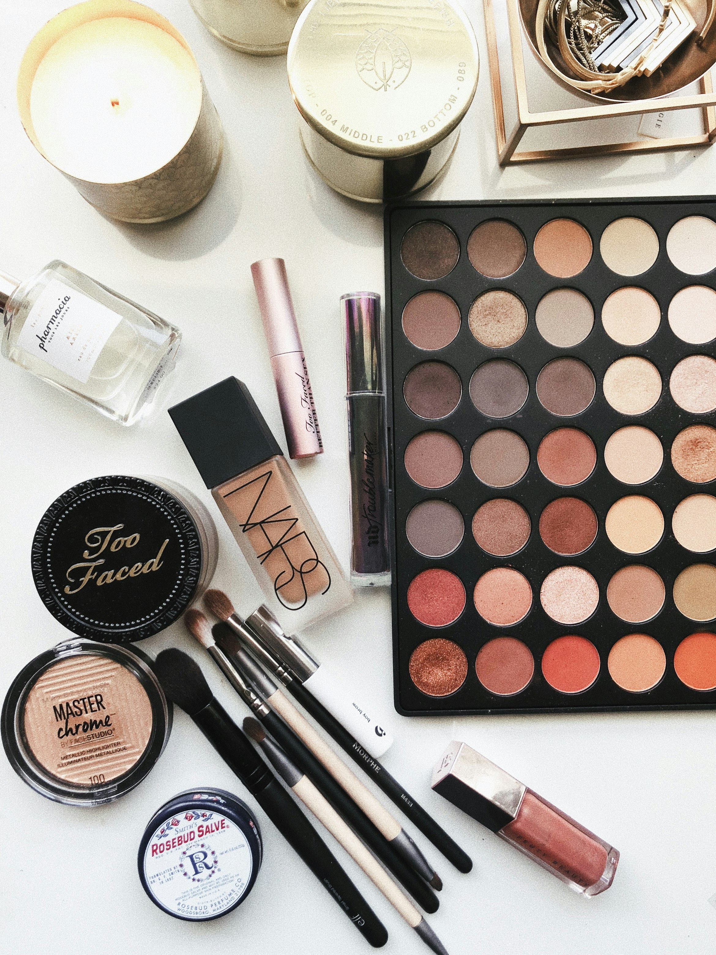 Professional makeup collection flatlay featuring eyeshadow palette, NARS foundation, brushes and various beauty products